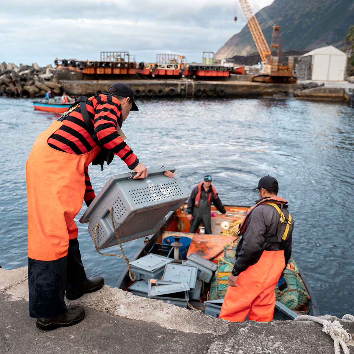 Fishermen in bright orange gear load a boat with traps.