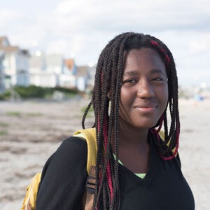 A young woman on a beach wearing a backpack in Maine.